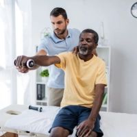 A male assisting a senior man in doing some exercises