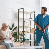 A male caregiver cleaning the room of a senior woman