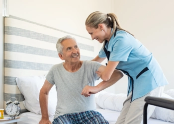 A female caregiver assisting a senior man to stand