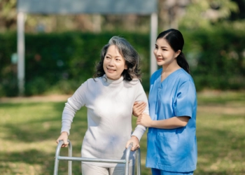 A female caregiver assisting a senior woman to walk outside