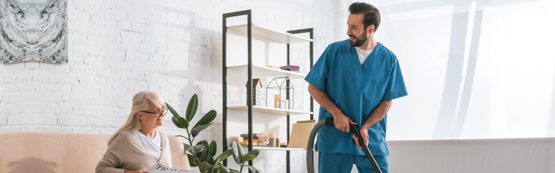 A male caregiver cleaning the room of a senior woman