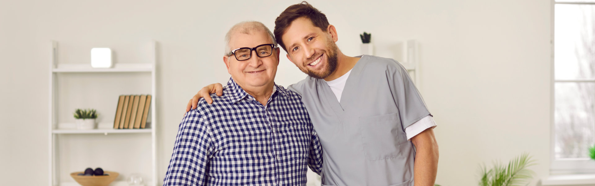 A senior man and a male caregiver putting their arms on each other's shoulder